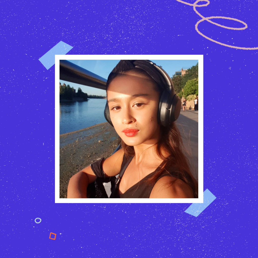 A selfie taken by Dr. Camila Pang. Pang wears headphones and a tanktop and is outside on a walking path near a river.