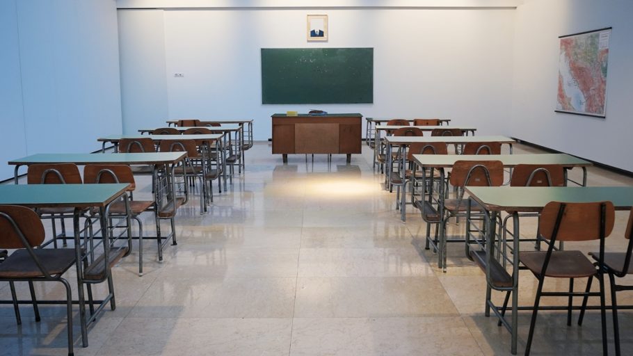 Interior de uma sala de aula de ensino primário, com a lousa apagada e as mesas vazias.