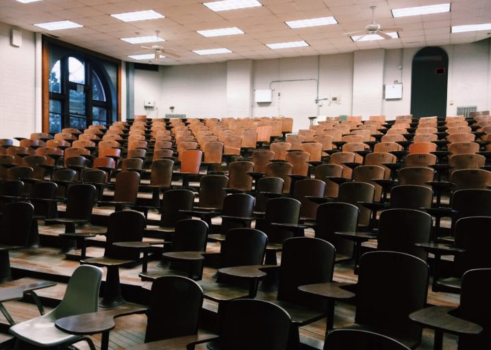 Interior de um auditório universitário com diversas cadeiras de madeira vazias.