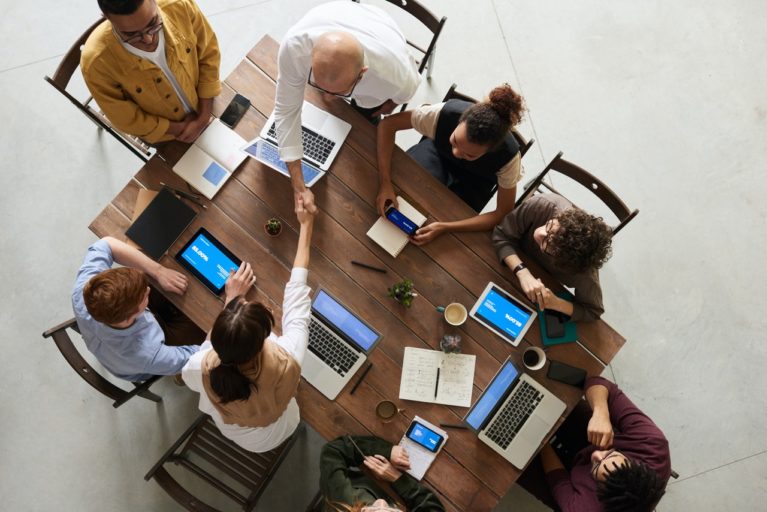 Foto vista de cima de uma mesa e várias pessoas sentadas em volta com seus computadores discutindo o que é a BNCC.