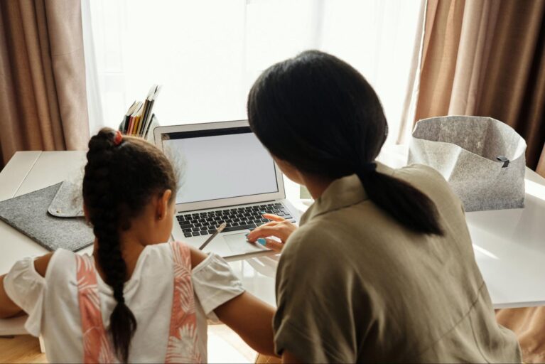 Em frente a um notebook, uma garota e sua mãe fazem tarefa de casa juntas.