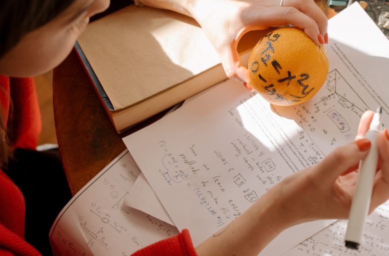 Menina estudando, anotando formulas matemática em uma laranja.