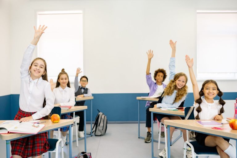 Sala de aula com seis estudantes levantando a mão na intenção de responder o professor(a). 