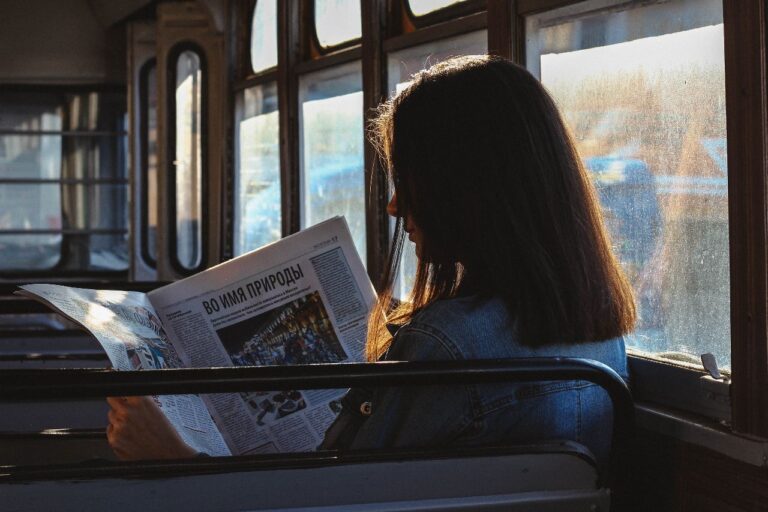 Mulher branca de cabelos lisos e curtos, lendo jornal no ônibus.