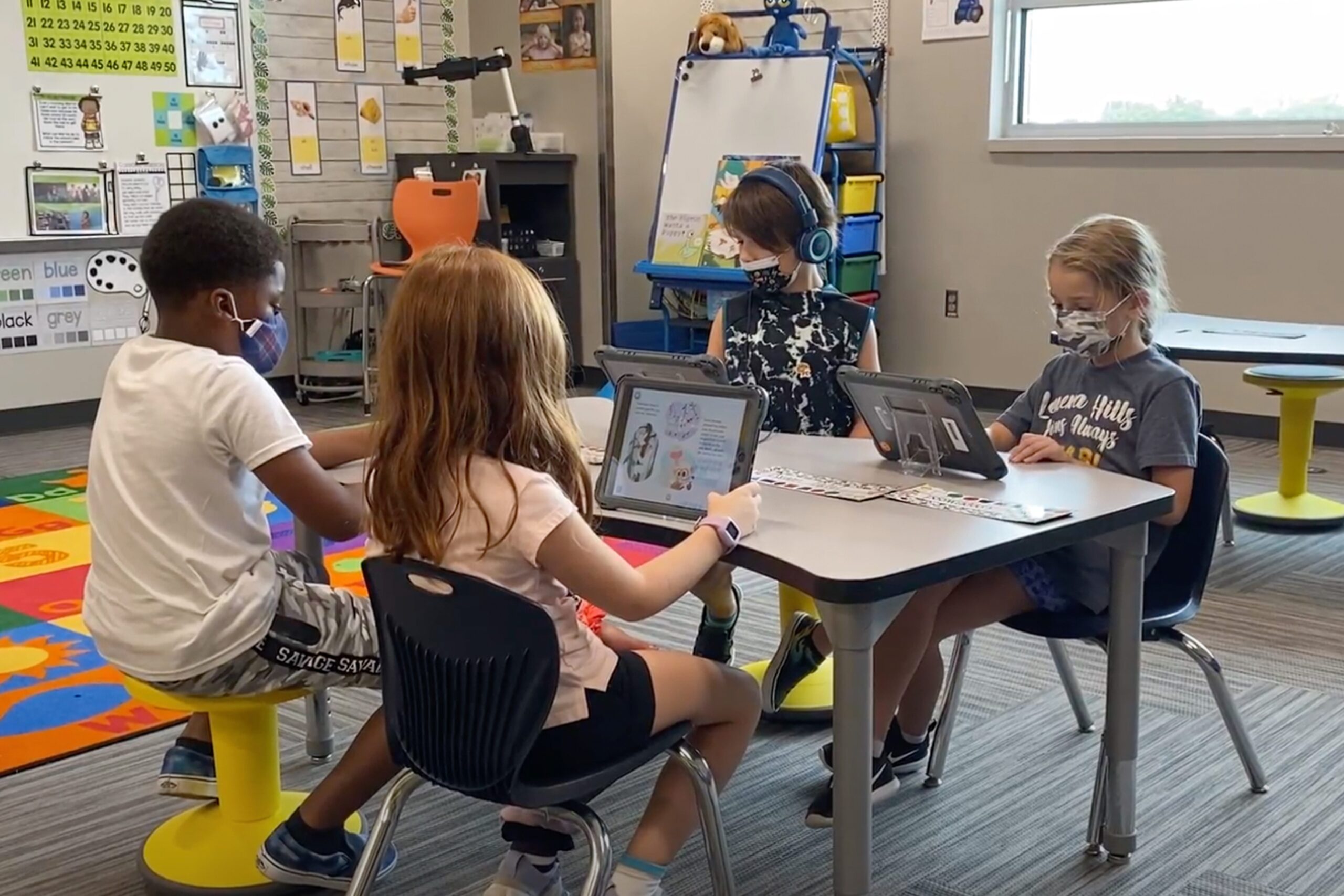 Four students use technology in the classroom during small groups. They are on their iPads, completely focused on independent work.