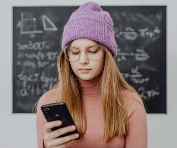 Garota jovem em frente lousa utilizando celular em sala de aula