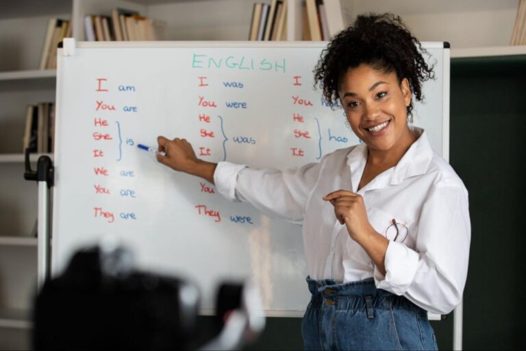 A imagem representa uma professora bilíngue em uma sala de aula, está anotando em um quadro branco. 