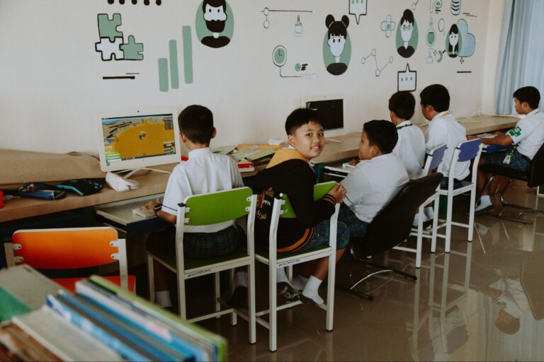 Em uma sala de aula, vemos alguns garotos sentados em um canto mexendo em computadores e um deles olha para trás, para a câmera.