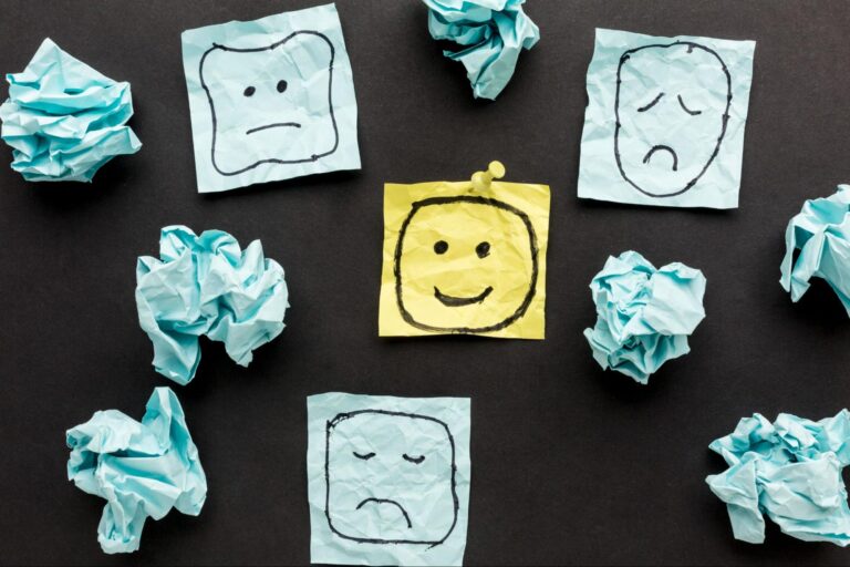  Na imagem há alguns papéis amassados na cor azul, onde três deles estão abertos com rostos tristes. Um deles, na cor amarela, está com um rosto feliz.