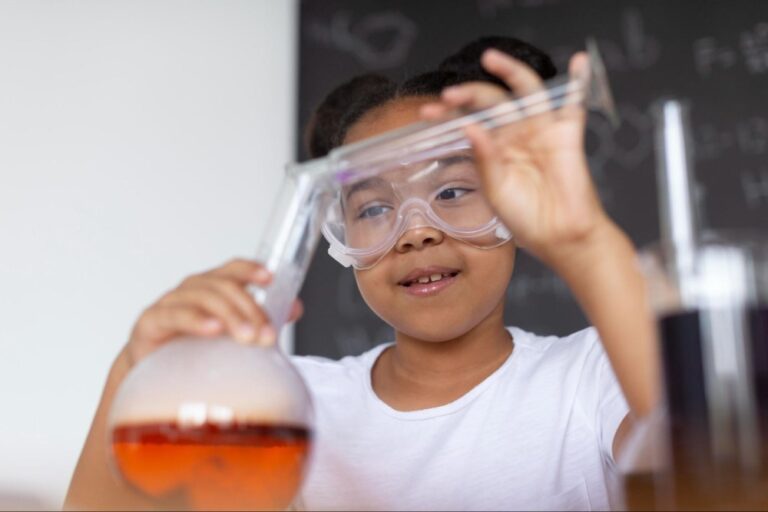 Criança está com óculos de proteção enquanto realiza um experimento em um laboratório