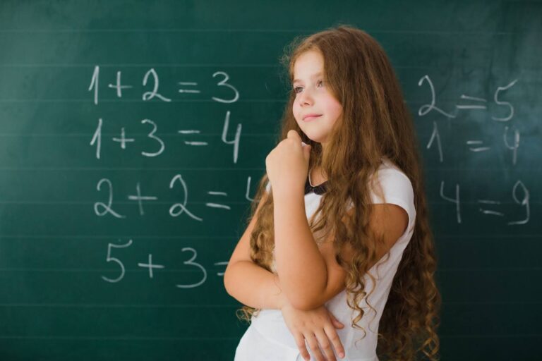 Menina de cabelos cacheados está em frente a uma lousa com números.